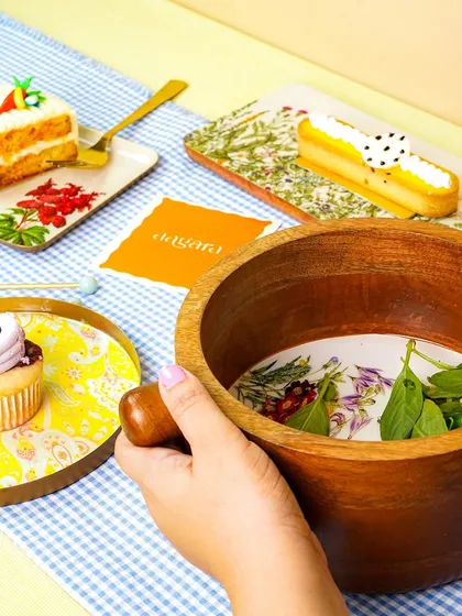 A close-up of a lifestyle scene, focusing on a hand holding a wooden bowl over a styled table.