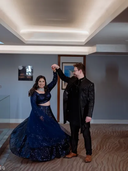A fun and dynamic shot of the couple sharing a dance. The bride's twirl shows off her sparkling blue lehenga, and their happy expressions capture the joy of the moment.