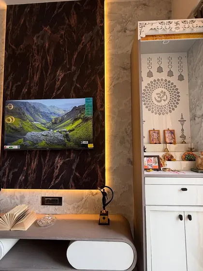 This living room corner features a striking TV unit with a dark marble accent wall and warm backlighting. Adjacent to it is a compact, elegant pooja unit, showing how we integrate different functional needs.