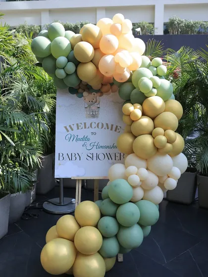 A welcome easel sign for a baby shower, framed by a lush balloon garland in shades of green and yellow. This is the first beautiful detail guests see when they arrive.