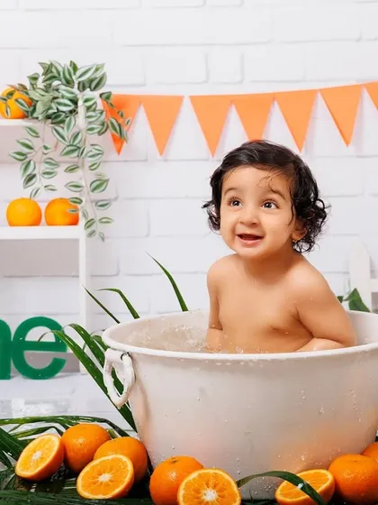 A baby boy enjoys a fun and refreshing tub splash surrounded by oranges and greenery.