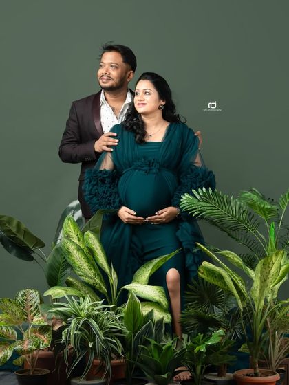 A confident and stylish pose surrounded by greenery. The dark teal gown stands out beautifully, creating a modern and chic pregnancy portrait for the expecting couple.