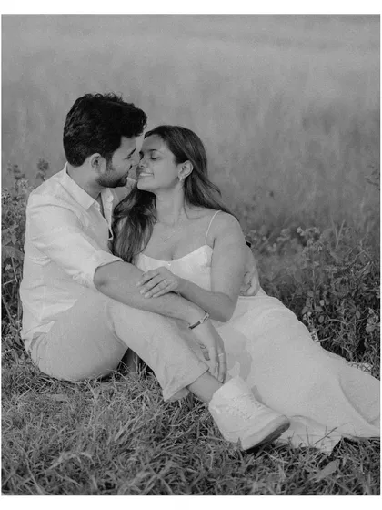 A soft and romantic black and white portrait of the couple sitting together in a field of grass, sharing an intimate moment.