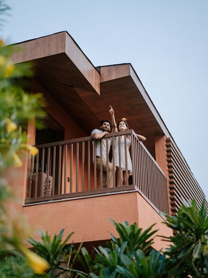 A couple shares a moment on their suite's balcony, surrounded by lush greenery. It is an ideal spot for quiet conversations and enjoying the pleasant Nandi Hills weather.