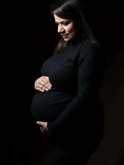 A simple and powerful low-key portrait of a mother-to-be in a black dress, focusing on the beautiful shape of her baby bump.