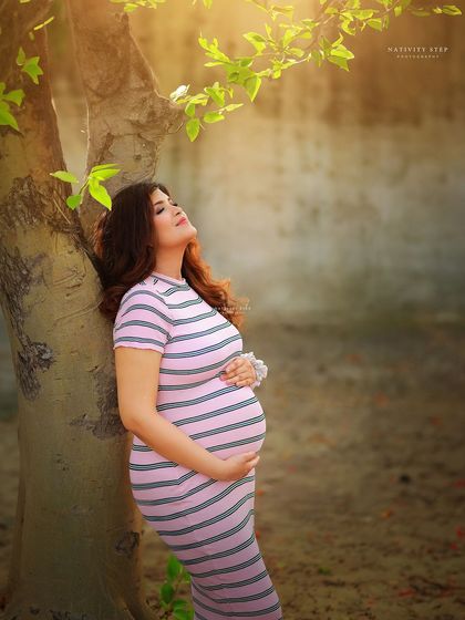 A peaceful moment of connection with nature. The mother-to-be leans against a tree, basking in the warm sunlight, creating a serene and beautiful image.