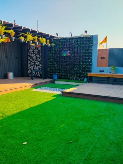 The Uttam Nagar project in daylight, showing the different textures of the artificial grass, wooden decks, and vertical garden wall.