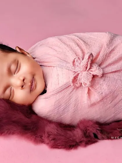A sweet smile from a baby wrapped in a pink swaddle, resting on a matching fuzzy rug. The simplicity of the setup keeps the focus on the baby.
