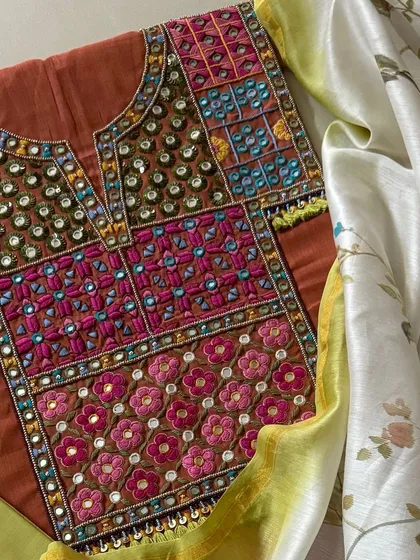 A striking combination of color and craft, this rust-colored handloom cotton kurta features a yoke of intricate thread and mirrorwork. It is paired with a delicate hand-painted silk chanderi dupatta adorned with whimsical bird and floral designs.