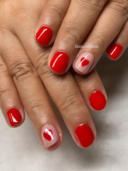 Simple, cute, and perfect for short nails. This classic red manicure is elevated with two accent nails featuring a sheer pink base and a single red heart.