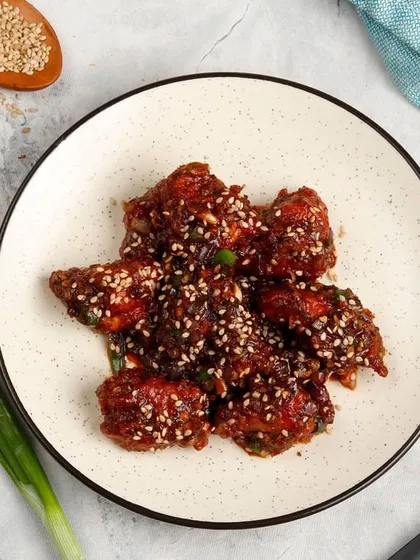 Our saucy Sesame Chicken, seen from a top-down angle. Bite-sized chicken pieces are coated in a thick, dark, and savoury sauce and generously sprinkled with sesame seeds.