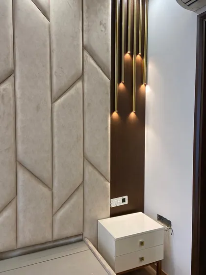 A work-in-progress shot of a custom bed back paneling. This design features geometric upholstered panels in a neutral fabric, paired with a dark wood accent and cascading pendant lights. This shows our attention to detail in creating unique and stylish headboards.