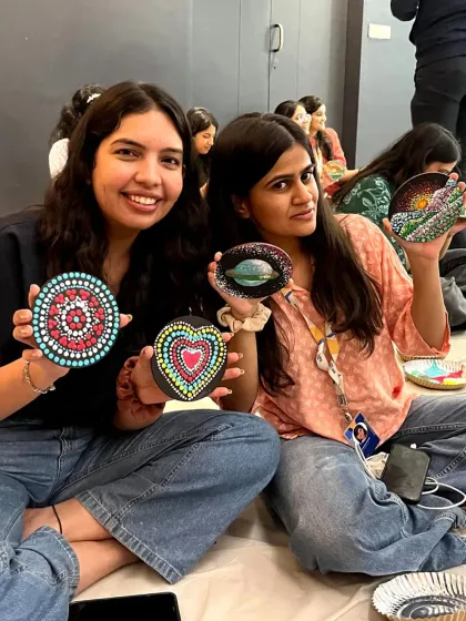 Two colleagues display the beautiful mandala dot art they created on stones during a team-building session. It's a relaxing and mindful activity perfect for de-stressing.