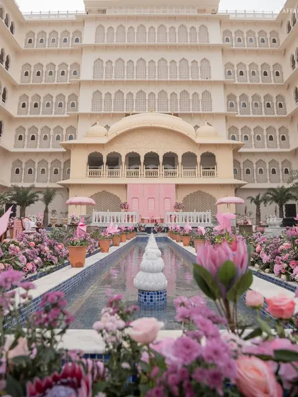 The stunning view of the Mehendi setup at Anantara Jaipur, with a long water body lined with pink florals leading towards the palace-like venue.