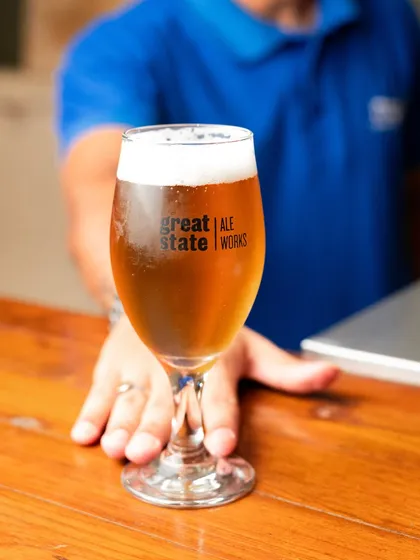 A freshly poured glass of craft beer being served over a wooden bar. The shot feels welcoming and focuses on the beautiful color and frothy head of the beer.