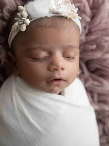 A peaceful close-up of a swaddled newborn, showcasing the delicate floral headband and the soft textures used in the session.