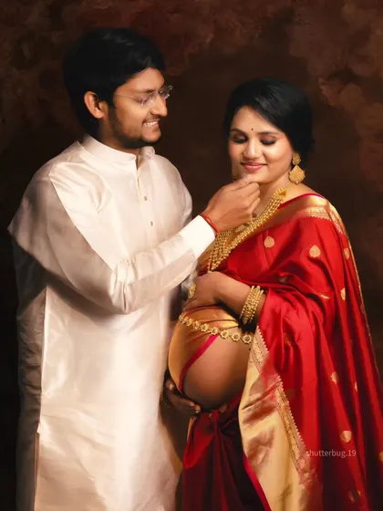Celebrating motherhood with traditional elegance, this couple's portrait is rich in cultural beauty. The vibrant red saree, gold jewelry, and the gentle interaction make this a warm and intimate traditional maternity photograph.