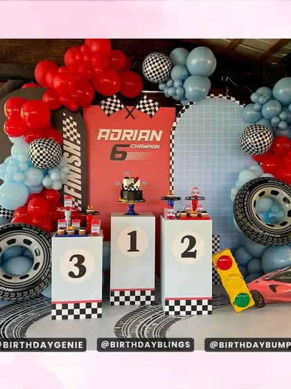 This race car theme for a 6th birthday features a winner's podium, large tire props, and a finish line backdrop. The red and blue color scheme is classic and exciting.
