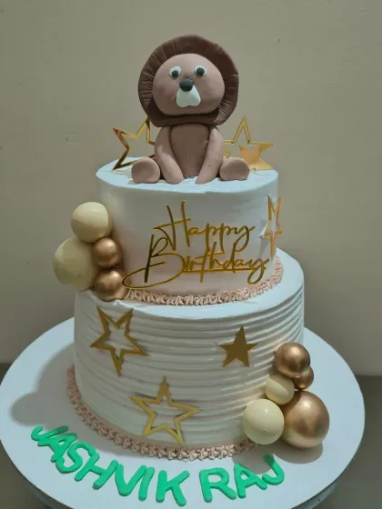 A two-tier birthday cake with a fondant lion topper and gold star decorations.