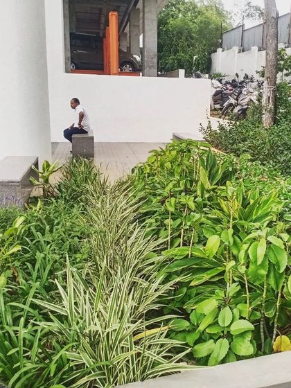 A quiet moment of rest in an industrial landscape. A simple bench is nestled within a dense garden bed, providing a peaceful spot for a break, surrounded by a variety of plant textures and forms.