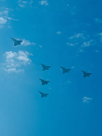 A formation of six fighter jets in a V-shape against the clouds.