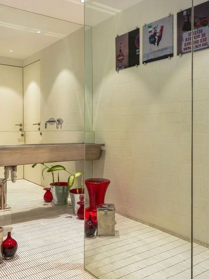 This washroom for a luxury Italian fashion showroom is a stylish dance of red, black, and chrome. Cleverly positioned mirrors and a statement steel-finished sink create a glamorous, high-fashion experience.