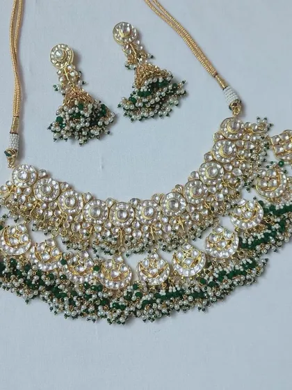 A beautiful Kundan choker with green and white beads, laid out to show its crescent shape. This rental set comes with matching jhumka earrings.