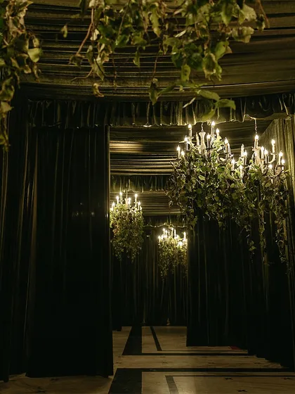 A grand gateway draped in opulent dark fabrics and lit by cascading chandeliers. This entrance sets a dramatic and luxurious tone for an unforgettable evening celebration.