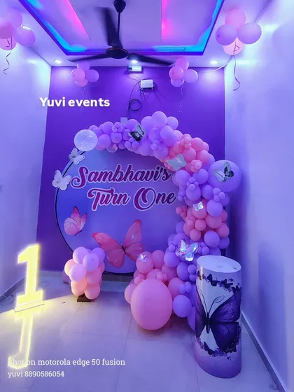 A butterfly-themed first birthday decoration for a home party. I used a round backdrop with purple and pink balloons and a light-up number '1' to fit the space perfectly.