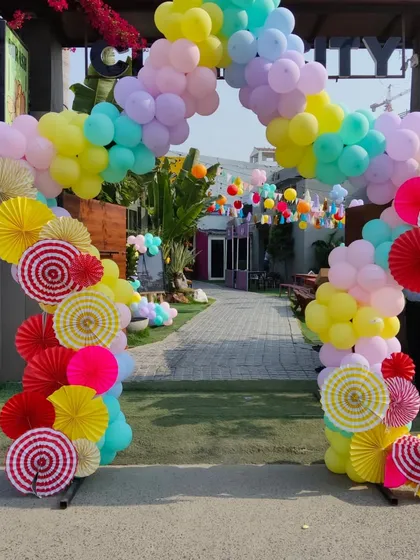 A vibrant and colorful balloon arch decorated with paper fans, creating a unique and festive entrance for a birthday party.