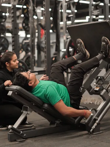 Our trainers are here to support everyone. A female trainer assists a member on the leg press, ensuring he maintains proper form and gets the most out of the exercise.