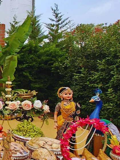 A beautiful decor setup featuring traditional dolls, a peacock figure, and trays of fruits and nuts, adding a touch of culture and artistry to the event space.