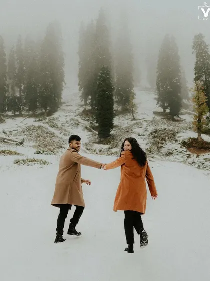 A couple joyfully runs through a snowy landscape in Kashmir, holding hands and looking back at the camera. This playful moment captures the fun and adventure of a destination pre-wedding photoshoot.