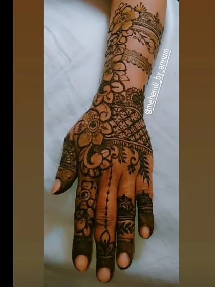 This full-hand design combines a variety of techniques, from the net pattern on the back of the hand to the floral bands on the arm and the delicate chain connecting the finger to the main design.