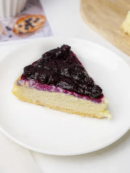 A slice of cheesecake with a rich blueberry compote topping. The contrast between the dark purple topping and the light cheesecake is visually appealing in this clean shot.