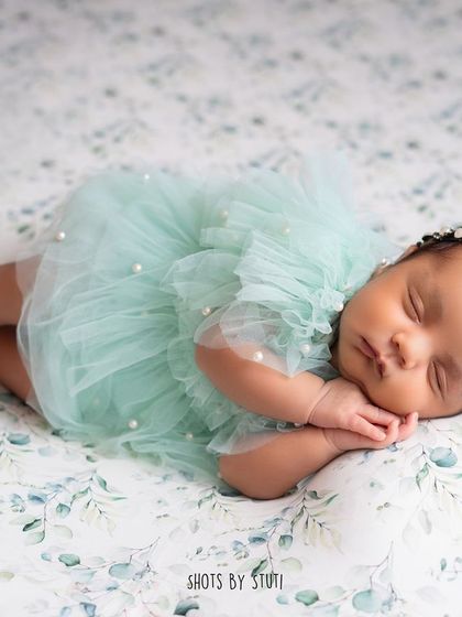 This little one is dreaming sweet dreams in a lovely mint-colored dress. The gentle smile on a sleeping newborn's face is one of the most precious things to capture.