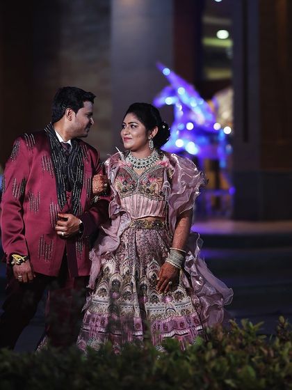 A happy couple at their reception. The groom wears our custom-designed burgundy tuxedo with intricate black embroidery, a perfect complement to his bride.