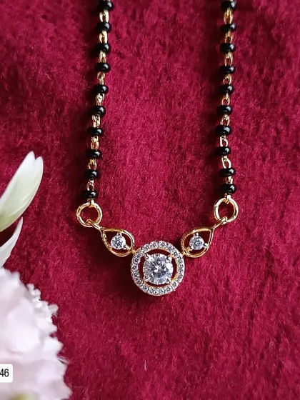 This modern mangalsutra design features a central solitaire-style American diamond in a circular halo setting. It's a classic and timeless piece, crafted from 92.5 silver with gold plating.