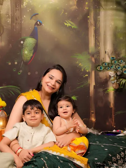 A mother sits with her two children, a toddler and a baby, during a festive Janmashtami photoshoot. This image is a beautiful portrait of a growing family and a mother's love for her children.