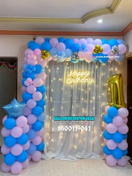 A classic first birthday decoration perfect for a home celebration. The pink and blue balloon arch, "Happy Birthday" neon sign, and a large number "1" foil balloon create a festive and joyful backdrop.