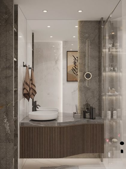This bathroom is a seamless blend of sophistication and serenity, defined by its pristine white and grey marble surfaces. Brushed gold fixtures introduce a warm, luxurious contrast, while an illuminated, rounded-edge mirror becomes a soft focal point.