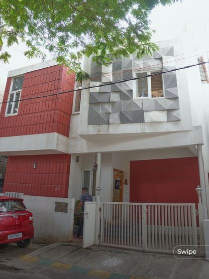 The facade of the Raghavendra Residence features a dynamic play of textures, with red terracotta blocks contrasting against a geometric grey panel, creating a unique and modern street presence.