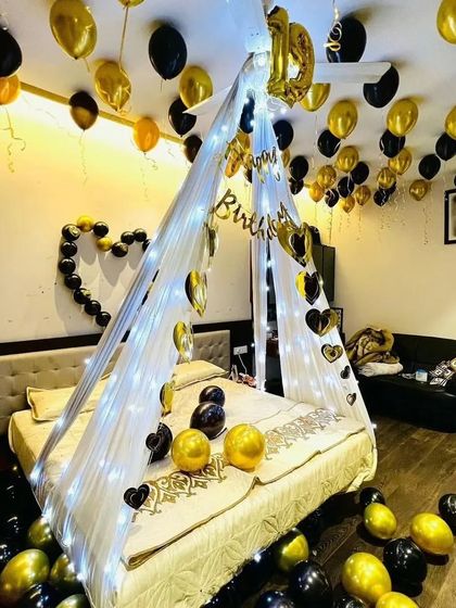 A birthday cabana setup in black and gold, featuring a fairy light canopy, heart-shaped wall decor, and balloons on the floor and ceiling.