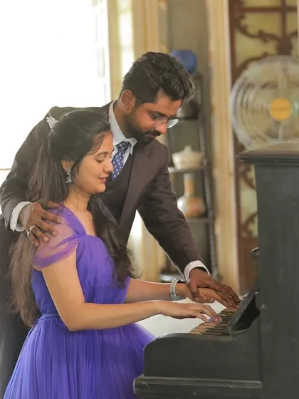 A sweet and romantic pre-wedding photo at a piano. The deep purple gown with a ruffled trail adds a touch of classic elegance to the scene.