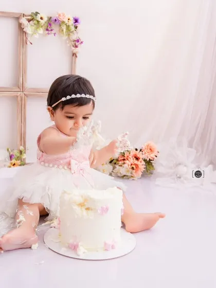 This little princess in her tutu is delicately exploring her first birthday cake, surrounded by a soft, dreamy floral setup.