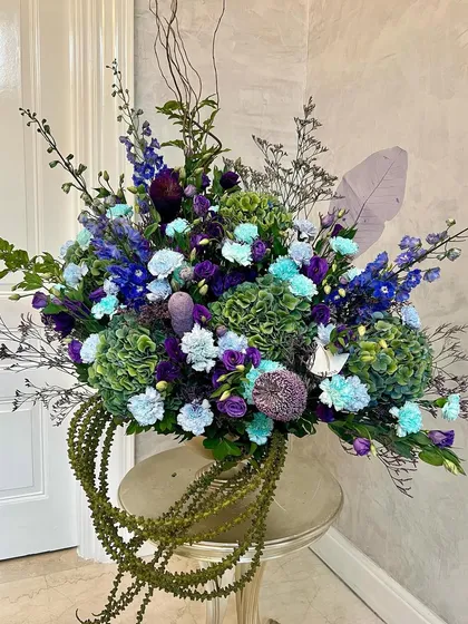 Immaculate and incredibly chic, this arrangement in sea green and deep purple communicates harmony with the eloquence of flowers. The cascading string-of-pearls succulent adds a unique, modern touch to the classic beauty of hydrangeas and delphiniums.