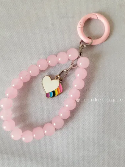 Sweet like cotton candy. This pastel pink beaded charm features a rainbow heart, adding a pop of pride and color to your phone, bag, or keys.