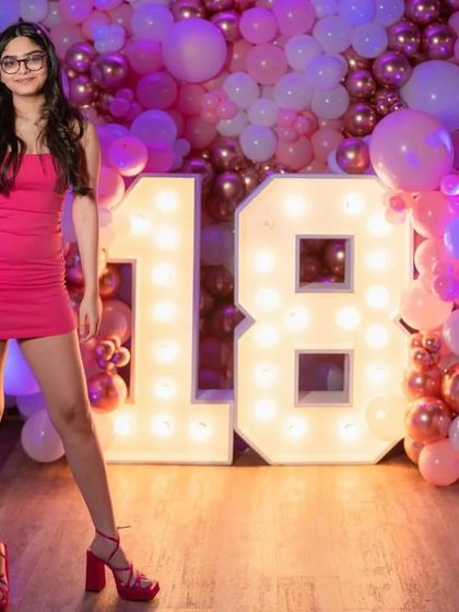 An 18th birthday celebration featuring a beautiful pink and rose gold balloon wall. The large, illuminated marquee numbers create a perfect focal point for photos and make the birthday girl the star of the show.