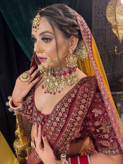 This editorial-style shot captures a regal bridal look. The model is wearing a deep maroon velvet lehenga with pink-toned eyeshadow and heavy kundan jewelry.