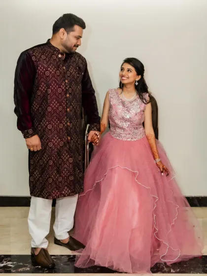 A full-length shot of the couple in their evening wear. The bride's layered pink gown is beautifully captured as they share a look.